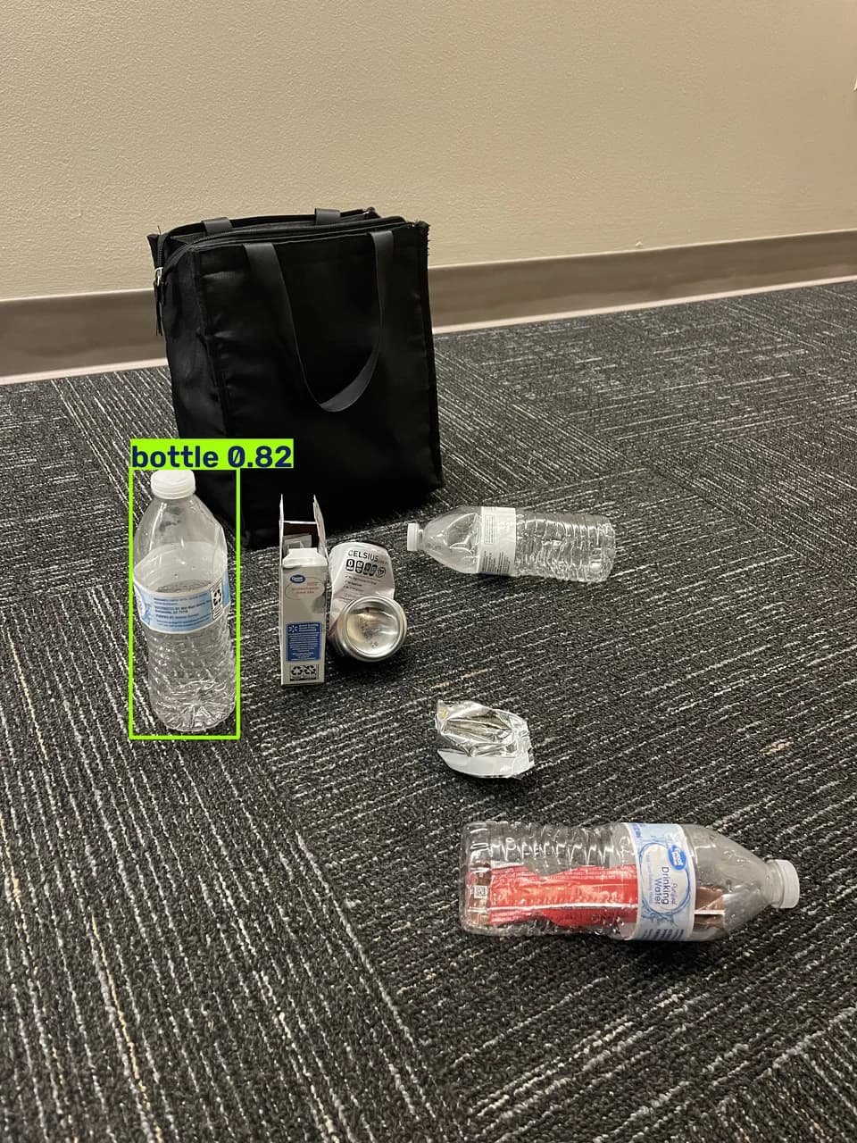 A group of bottles, packaging, and a can beside a black bag; one upright bottle is boxed and labeled bottle 0.82.